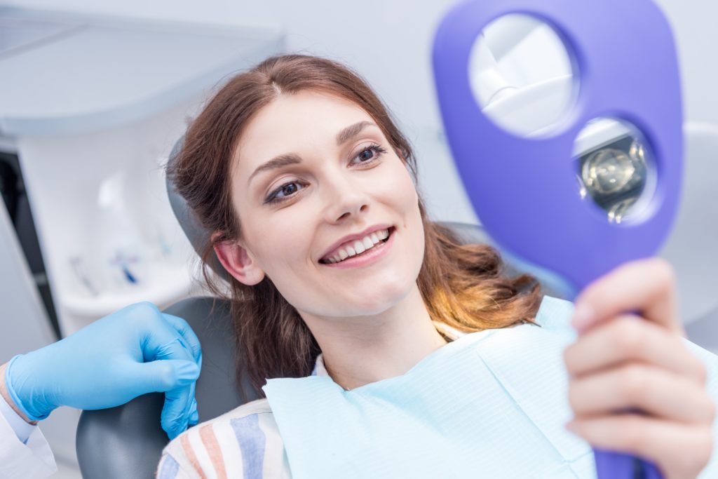 Junge Frau prüft mit einem Spiegel ihr Lächeln nach einer Zahnbehandlung