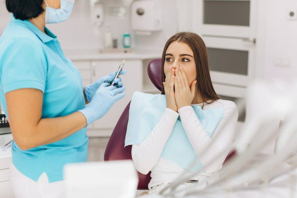 The dentist injects anesthesia to the girl patient, she is scared.